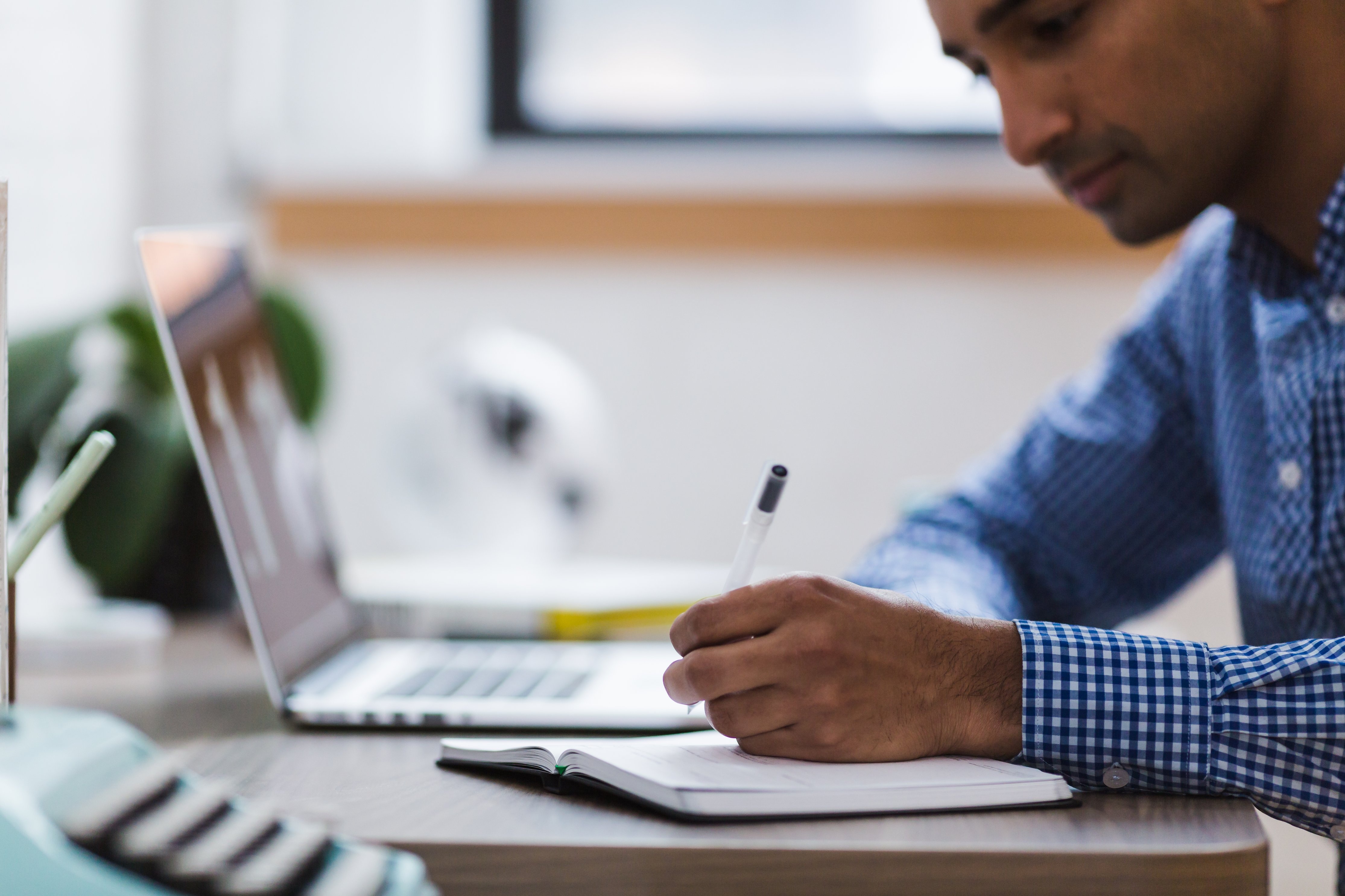 man writing in notebook next to computer